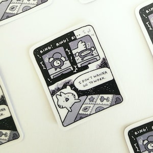 May include: Black and white comic strip sticker featuring a cat in bed, with an alarm clock ringing and the text "RING! RING! RI- ... I DON'T WANNA GO TO WORK."