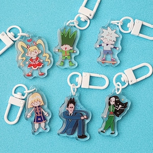 May include: Six colourful cartoon character keychains with white metal rings. The characters include a girl with pigtails, a boy with green hair, a boy with white hair, a boy with blonde hair, a man in a suit, and a girl with long black hair.