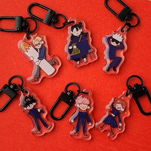 May include: Set of ten colorful keychains featuring cartoon characters. Each keychain has a black metal ring and a clear acrylic charm with a different character design.