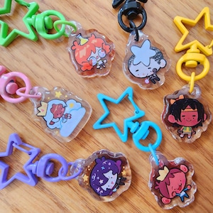 May include: A set of ten colorful star-shaped keychains with different cartoon characters. Each keychain features a clear plastic charm with a colorful cartoon character design.