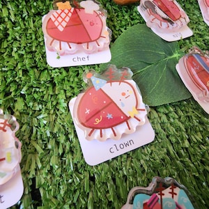 May include: A set of ten colorful, cartoon-style ladybug pins. Each pin features a different character, such as a chef, a clown, a sailor, and a maid. The pins are made of clear plastic with a red and white design. The text on the cards reads "chef", "clown", "sailor", "maid", "bathtime", and "artist".