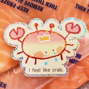 May include: A holographic sticker featuring a cartoon crab with a crown, crying, and the text "I feel like crab." The crab is red, pink, and yellow with a glittery border. The sticker is on a clear plastic bag.