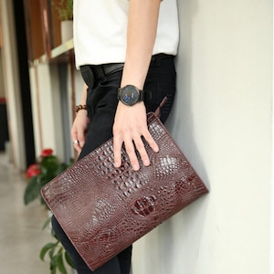 May include: A brown leather clutch with a crocodile pattern. The clutch has a zip closure and a strap.