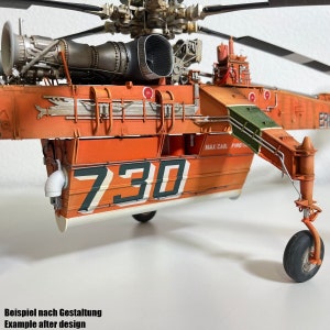 Könnte beinhalten: Eine Nahaufnahme eines orangefarbenen und grünen Hubschraubermodells mit der Nummer "730" auf der Seite. Der Hubschrauber hat einen großen Motor und einen langen, beweglichen Ausleger.