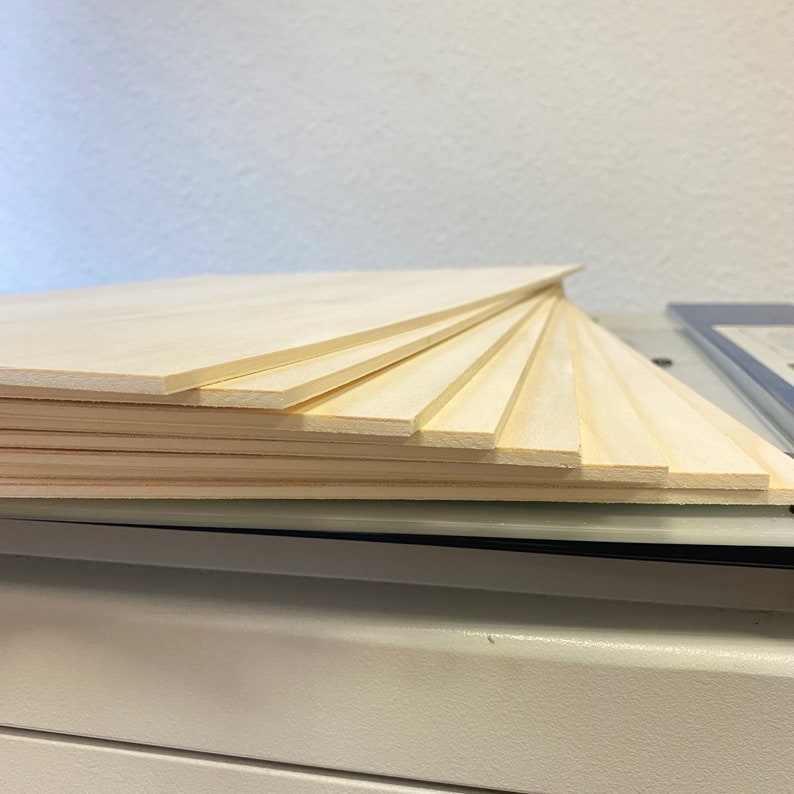 May include: A stack of thin, light wood boards, likely plywood, with a smooth, natural finish. The boards are stacked in a staggered pattern, creating a visual texture.
