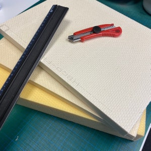 Peut inclure: Trois plaques de mousse, une blanche, une jaune et une beige, sont empil&eacute;es sur un tapis de coupe vert. Une r&egrave;gle noire et un couteau utilitaire rouge sont pos&eacute;s sur les plaques de mousse.