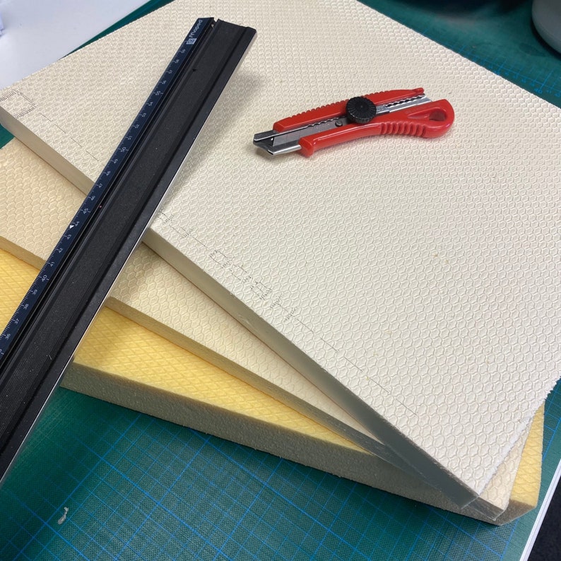 Peut inclure: Trois plaques de mousse, une blanche, une jaune et une beige, sont empil&eacute;es sur un tapis de coupe vert. Une r&egrave;gle noire et un couteau utilitaire rouge sont pos&eacute;s sur les plaques de mousse.