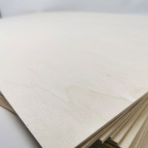 May include: A stack of light-colored wood veneer plywood sheets. The top sheet is smooth and has a subtle grain pattern.