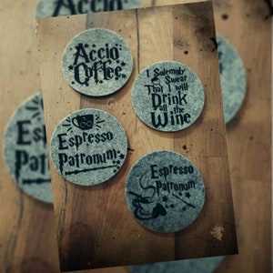 May include: Four gray felt coasters with black text and images. The coasters feature Harry Potter themed sayings, including "Accio Coffee", "I Solemnly Swear That I Will Drink All The Wine", and "Espresso Patronum".