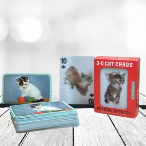 May include: A selection of cat-themed items, including a deck of playing cards, a stack of cards with a cat image, and a red box of 3-D cat cards. The cards feature images of kittens. The box reads "3-D CAT CARDS".
