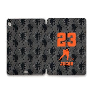 May include: A black and gray iPad case with a hockey player graphic and the number 23 in orange. The text "Jacob" is printed below the number. The background is a repeating pattern of hockey players.