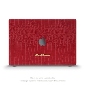 May include: A red laptop case featuring a crocodile skin effect. The Apple logo is centrally placed, with the name "Mary Thompson" in gold script. The text below reads, "This is not a real crocodile skin. The design is printed on the case surface without textures."