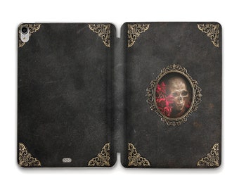 May include: A black leather iPad case with a gold ornate design. The front cover features a skull with red flowers in a gold frame.