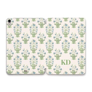 May include: A tablet case featuring a repeating pattern of blue and green floral motifs on a cream background. The right side of the case displays the letters KD in a green serif font. The case includes a circular camera cutout on the top left.
