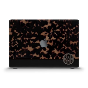 Może przedstawiać: Czarny laptop z wzorem imitującym pancerz żółwia i czarną wstążką u dołu. Logo Apple jest widoczne w lewym górnym rogu. Inicjały "EMB" znajdują się w kółku po prawej stronie laptopa.
