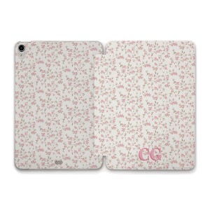 May include: An open tablet case with a floral pattern in pink and gray on a white background. The case has a monogram in the lower right corner. The case is designed to protect the tablet.