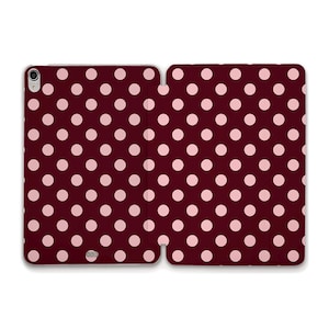 May include: A burgundy tablet case with a pink polka dot pattern. The case is open, revealing the interior and exterior design. The polka dots are evenly spaced across the surface.