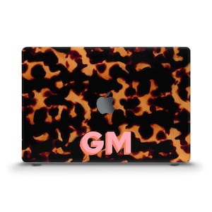 May include: A laptop case with a tortoiseshell pattern in shades of brown and black. The case features the Apple logo and the pink letters "GM". The case is designed to fit a laptop.