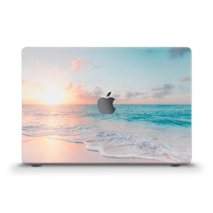 May include: A laptop skin with a beach sunset scene. The image features a sandy beach with turquoise water and a pink and orange sunset sky.