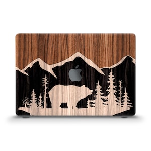 May include: A wood-grain laptop skin with a black silhouette of a bear, mountains, and trees. The skin has a wood-grain pattern and a black background.