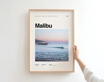 May include: A framed print featuring a Malibu surf spot. The print includes the text "UNITED STATES SURF SPOTS" and "Malibu" in bold black letters. The image shows a surfer in the ocean with a pier in the background, under a pastel sky.