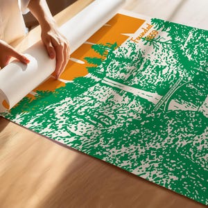 May include: A person unrolling a poster with a green and white landscape design, an orange sky, and the text "Founded 1859". The poster is on a wooden surface.