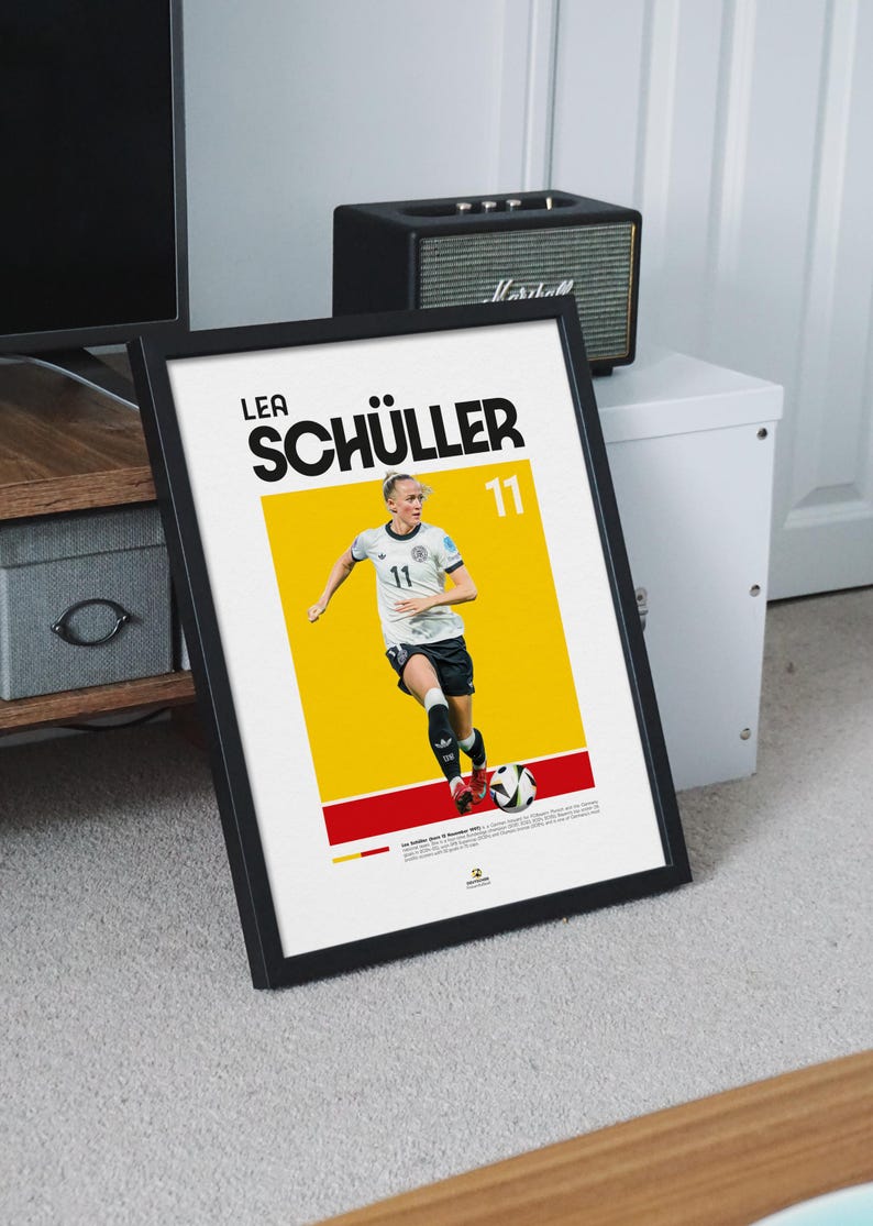 May include: Framed poster of Lea Sch&uuml;ller, a footballer, in action. The poster has a yellow and red background with the player's name and number 11 in bold text. The player is wearing a white and black uniform.