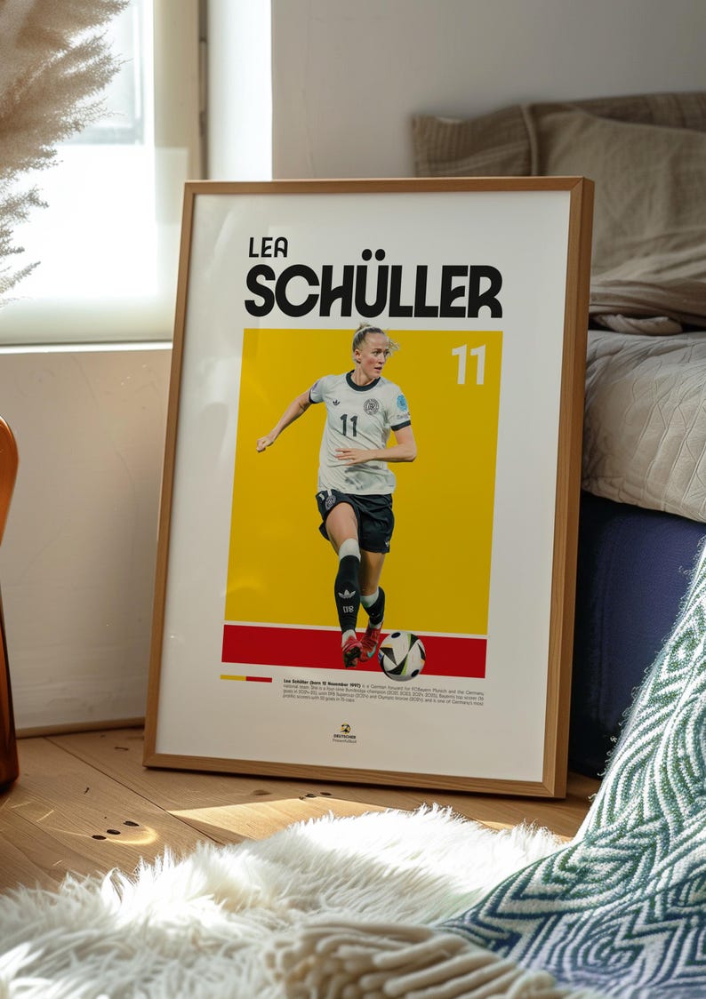 May include: Wooden framed poster of Lea Sch&uuml;ller, number 11, in a football uniform. The poster has a yellow background with the player's name in large black letters. The image is set in a room with a wooden floor and a white rug.