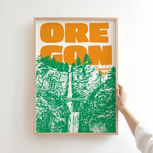 May include: A framed art print featuring the word "OREGON" in orange block letters above a green and white illustration of a waterfall and forest. The text "Founded 1859" is also present.