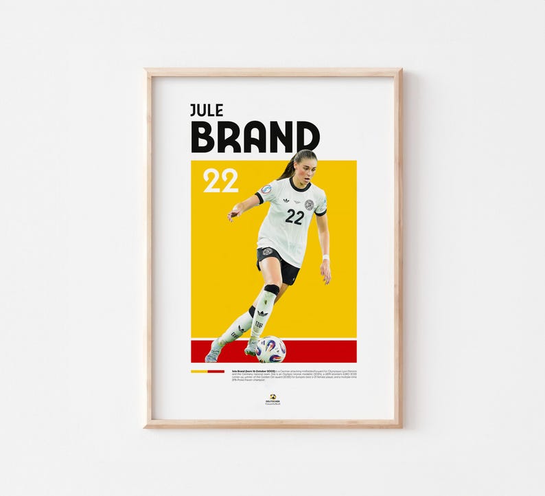 Może przedstawiać: Oprawiony plakat z piłkarką w biało-czarnym stroju, imieniem "JULE BRAND" i numerem "22" pogrubioną czcionką. Tło jest ż&oacute;łte i czerwone, z zawodniczką kopiącą piłkę nożną.