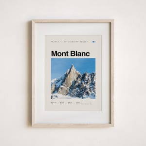 May include: Framed art print featuring a photograph of Mont Blanc, a snow-covered mountain peak under a clear blue sky. The print includes the text "Mont Blanc" in bold black letters, with additional text indicating climbing routes.