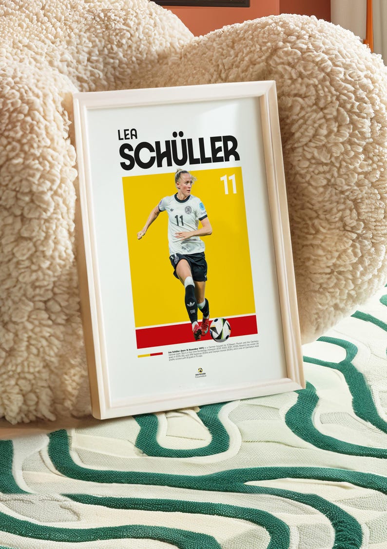 May include: Framed poster of footballer Lea Sch&uuml;ller in a white and black kit, number 11. The background is yellow and red. The poster is in a white frame, ideal for a sports fan's decor.