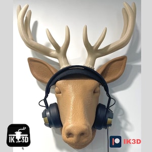 May include: A brown deer head mounted on a wall with black headphones on. The deer head has large antlers. The headphones have a black headband and earcups with gold accents.
