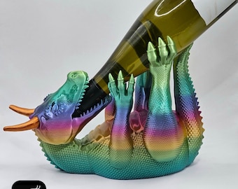 Puede incluir: Un porta botellas de vino con forma de dragón iridiscente arcoíris. El dragón sostiene una botella de vino en su boca.