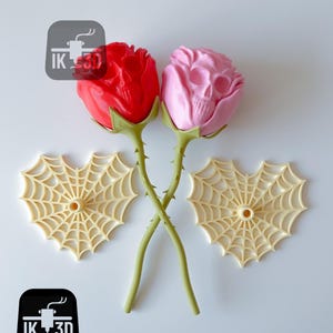 Puede incluir: Dos rosas decorativas, una roja y otra rosa, con un dise&ntilde;o de calavera. Los tallos verdes se cruzan. Tambi&eacute;n hay dos decoraciones de telara&ntilde;a beige. La imagen incluye el texto "IK 3D" en un cuadrado negro.