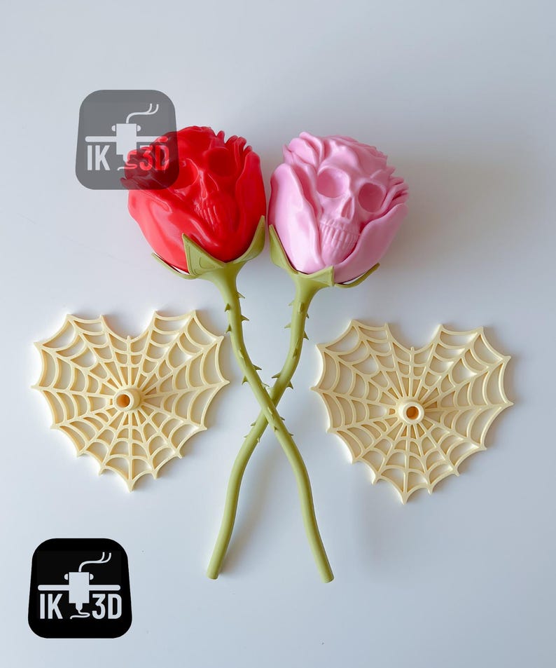 Puede incluir: Dos rosas decorativas, una roja y otra rosa, con un dise&ntilde;o de calavera. Los tallos verdes se cruzan. Tambi&eacute;n hay dos decoraciones de telara&ntilde;a beige. La imagen incluye el texto "IK 3D" en un cuadrado negro.