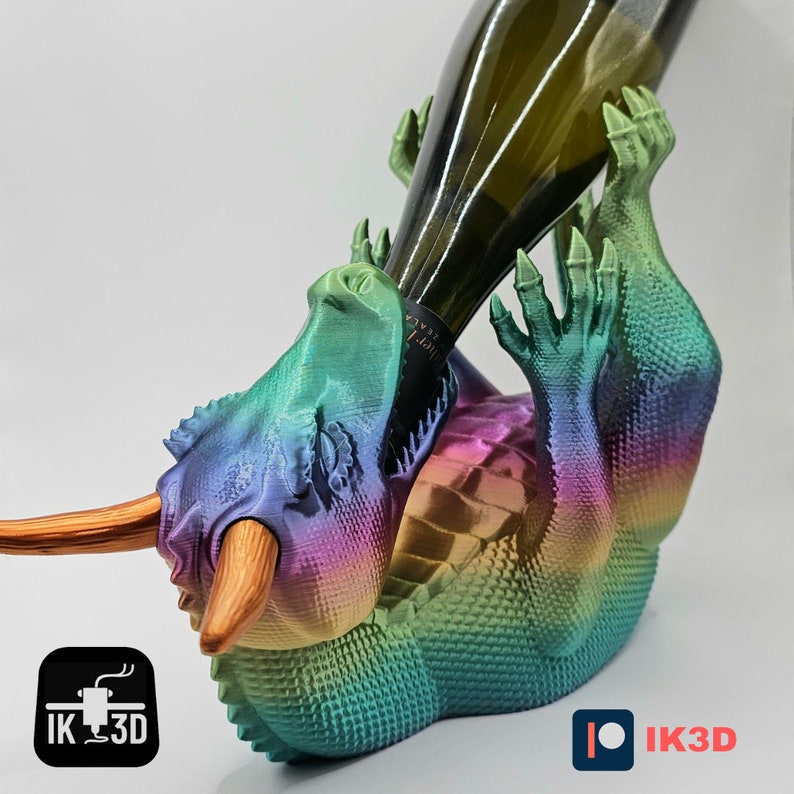 May include: A 3D printed iridescent dragon bottle holder with a bottle of wine in its mouth. The dragon is green, blue, purple, and gold.