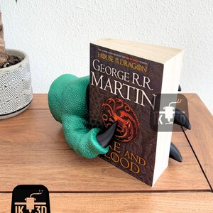 May include: Green and black dragon claw bookend holding a book titled "House of the Dragon" by George R.R. Martin. The book cover features a three-headed dragon.
