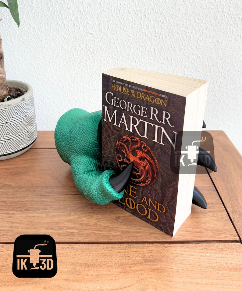May include: Green and black dragon claw bookend holding a book titled "House of the Dragon" by George R.R. Martin. The book cover features a three-headed dragon.