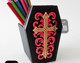 May include: Black coffin-shaped desk organizer with a red and gold cross design. The organizer is filled with colorful pencils. The design includes the text "IK 3D".