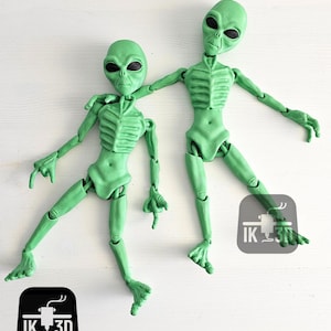 Puede incluir: Dos figuras alien&iacute;genas articuladas de color verde con cabezas grandes y ojos grandes. Las figuras est&aacute;n posadas de forma din&aacute;mica, con un brazo de una figura apoyado en el hombro de la otra. Las figuras est&aacute;n hechas de pl&aacute;stico liso verde.