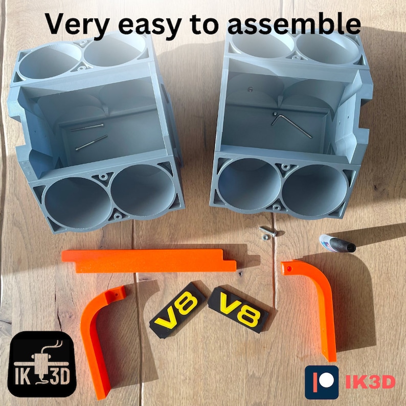 May include: A flat-pack, gray plastic model kit of a V8 engine. The kit is partially assembled and includes orange plastic parts, two black and yellow V8 labels, and small screws. The text "Very easy to assemble" is visible in the image.