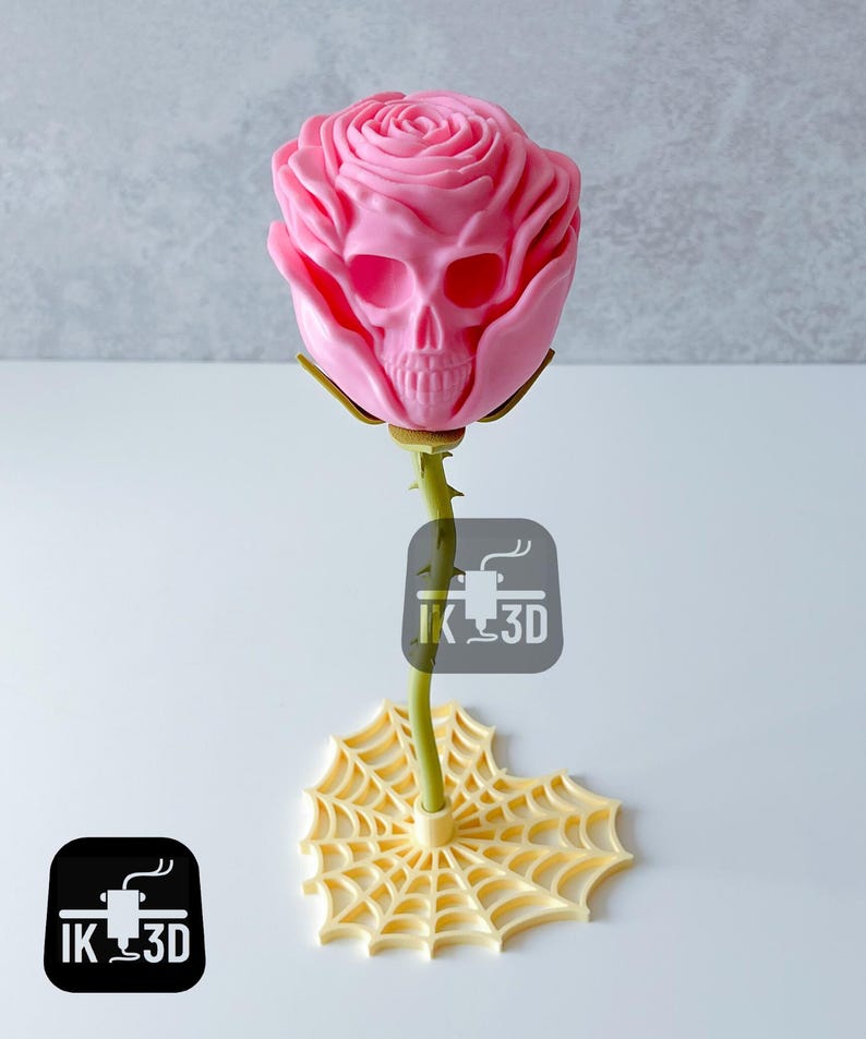 Puede incluir: Una escultura de rosa rosa con un dise&ntilde;o de calavera en el centro de la flor. El tallo es verde y la base es un dise&ntilde;o de telara&ntilde;a amarilla. El logotipo "IK 3D" es visible.