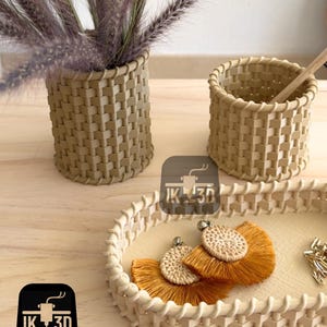 May include: Three woven baskets in a light brown color. The baskets are in different sizes and shapes. The largest basket is oval and has a woven design. The two smaller baskets are round and have a woven design. The baskets are on a wooden surface.