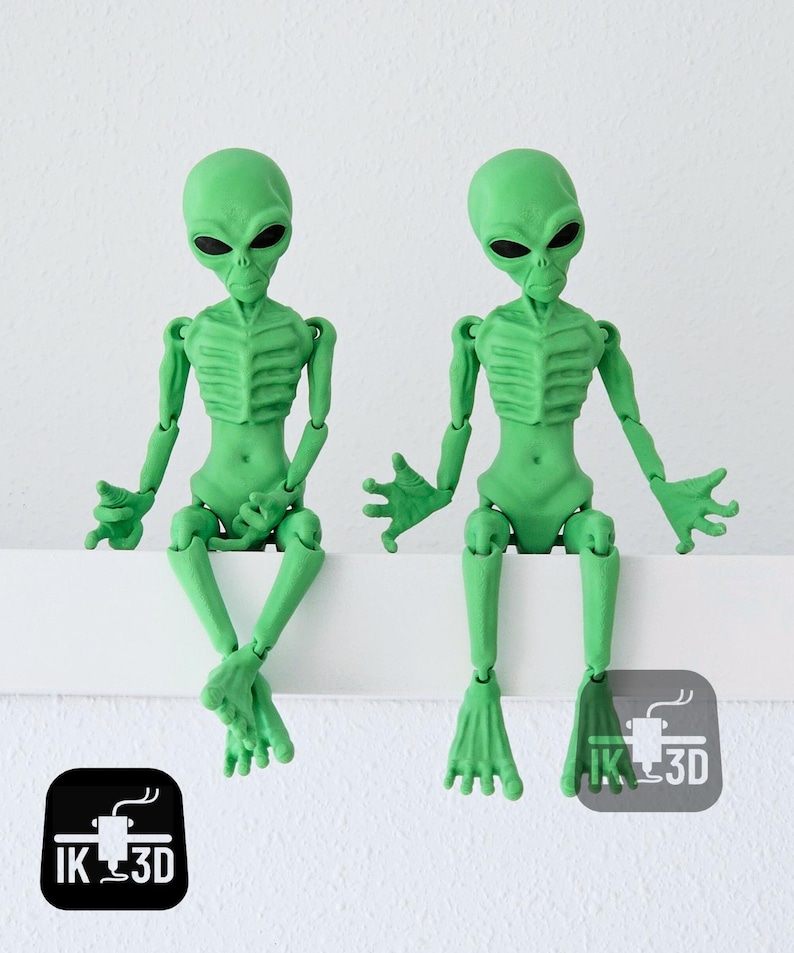 Puede incluir: Dos figuras de extraterrestres verdes con extremidades articuladas, sentadas sobre una superficie blanca. Los extraterrestres tienen cabezas grandes, ojos negros y estructuras esquel&eacute;ticas detalladas. Las figuras est&aacute;n impresas en 3D y tienen un acabado mate.