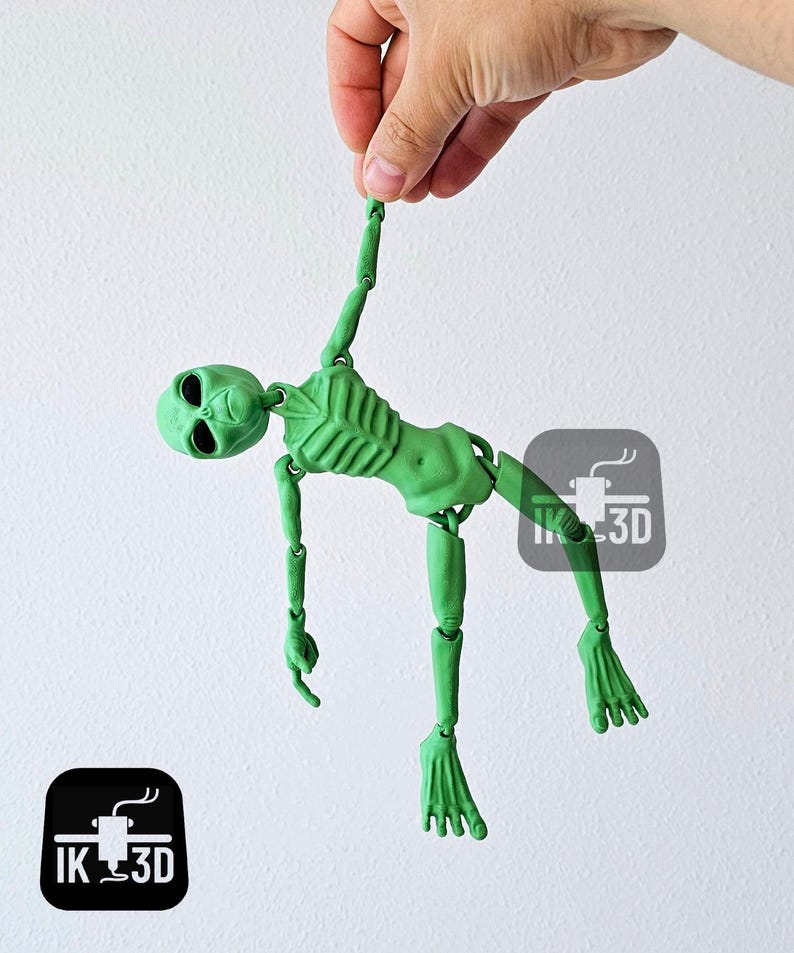 Puede incluir: Una figura de esqueleto de alien&iacute;gena verde articulada con una cabeza grande y extremidades largas. La figura est&aacute; en una posici&oacute;n colgante con los brazos y las piernas extendidos.