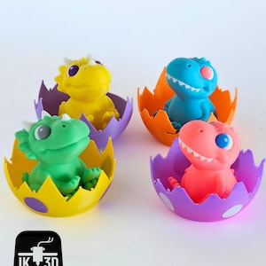 May include: Four brightly coloured dinosaur toys, each inside a cracked eggshell. The dinosaurs are yellow, blue, green, and pink, with white details. The eggshells are purple, orange, and yellow with white polka dots. The image includes the text "IK 3D".