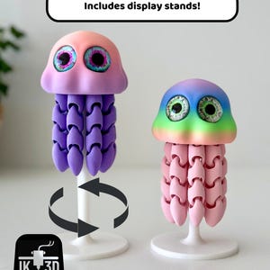 May include: Two colorful, 3D-printed jellyfish sculptures with display stands. One jellyfish is pink and purple, the other is pink and rainbow-colored. The text "Includes display stands!" is above the jellyfish.