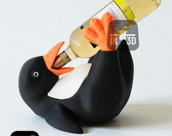 Puede incluir: Un soporte para botellas de vino con forma de pingüino en blanco y negro con pico y patas naranjas, que sostiene una botella de vino blanco. El pingüino tiene el vientre blanco y está tumbado boca arriba. La botella está inclinada hacia el pico del pingüino.