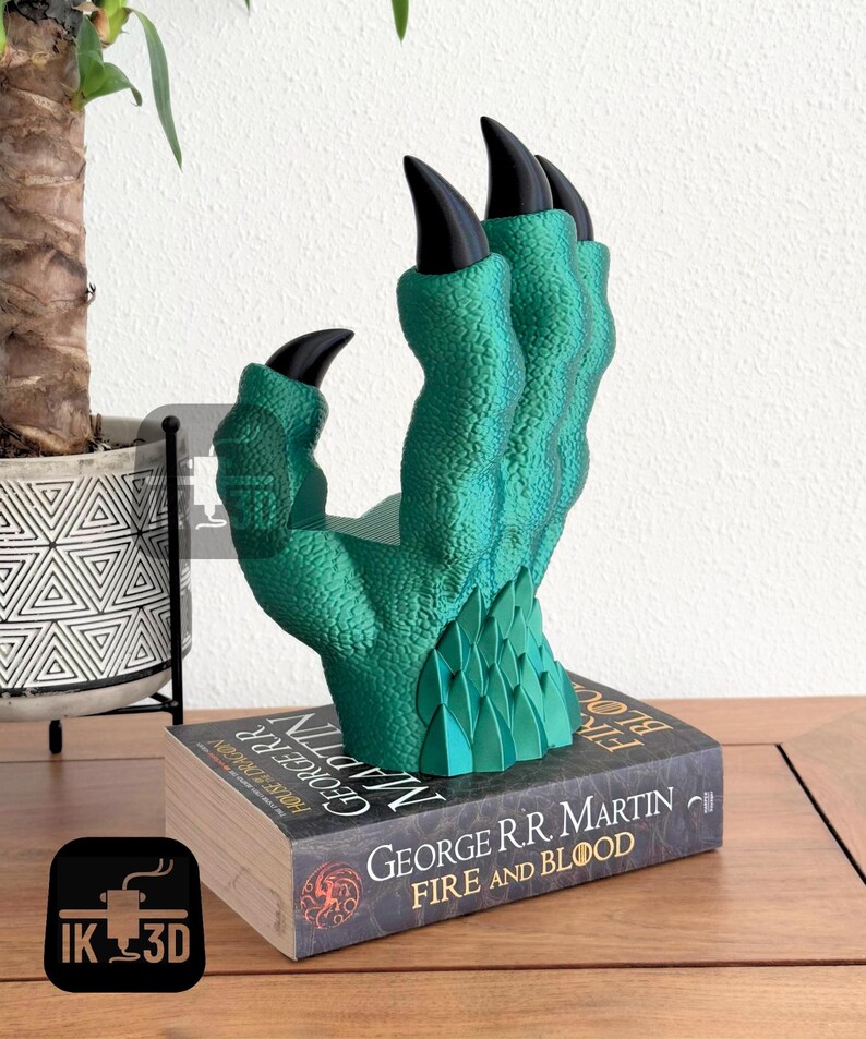 May include: A green dragon claw bookend with black claws, resting on a book titled "Fire and Blood" by George R.R. Martin.